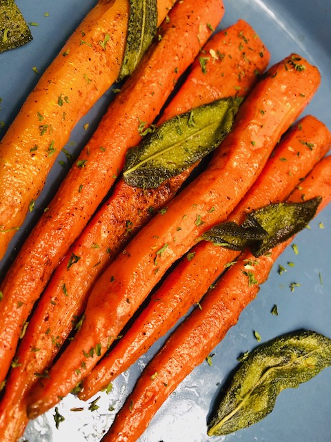 Brown butter sage carrots on a light blue plate topped with fresh sage leaves and sprinkled with dried parsley.